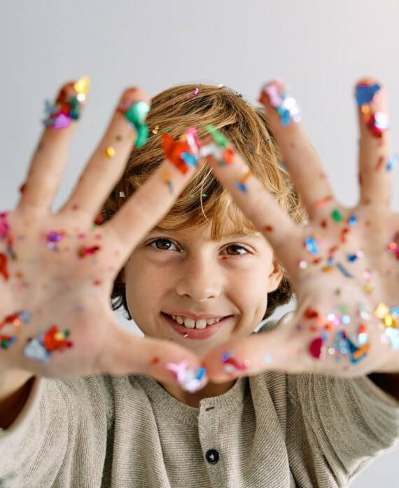 Positive kid showing hands with colorful confetti during party